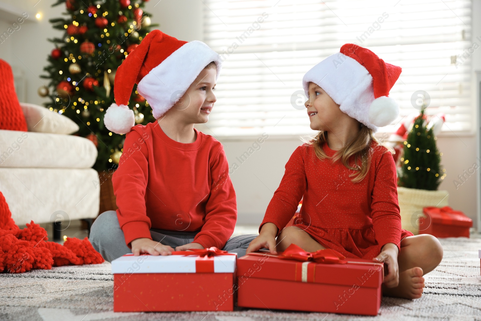 Photo of Happy little children in Santa hats with Christmas gifts on floor at home