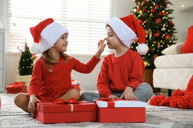 Photo of Happy little children in Santa hats with Christmas gifts on floor at home