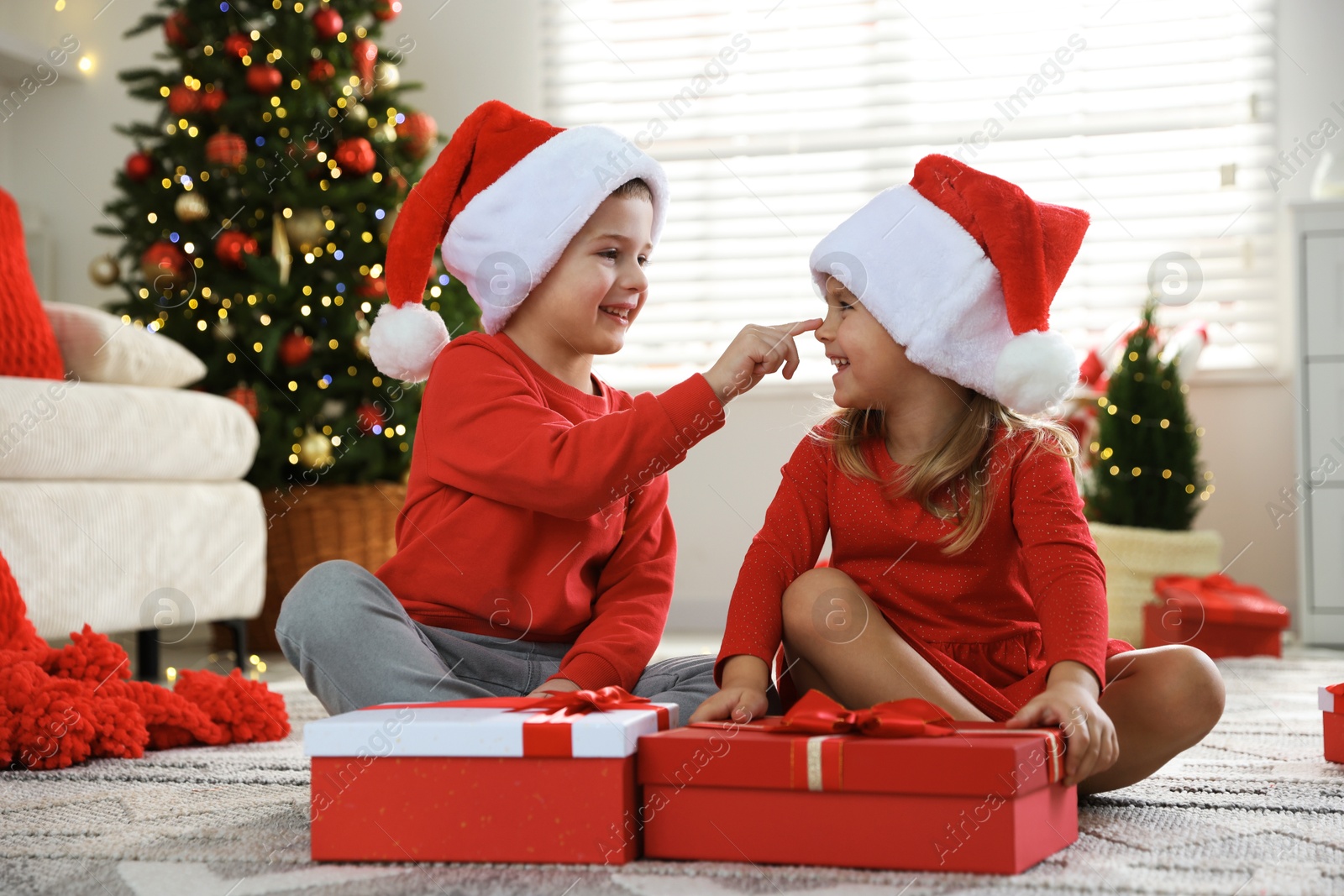 Photo of Happy little children in Santa hats with Christmas gifts on floor at home