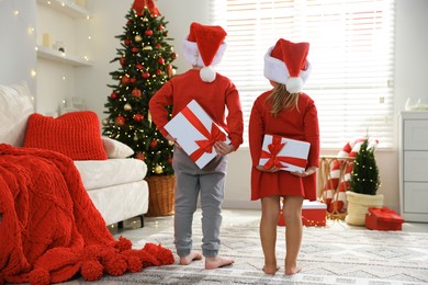 Photo of Little children in Santa hats with Christmas gifts at home, back view