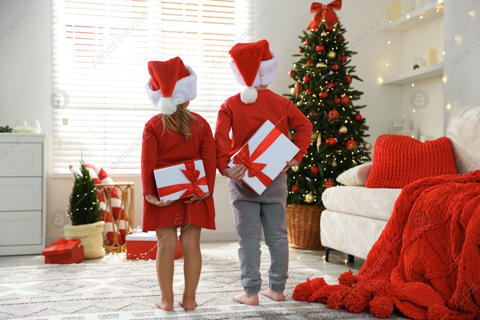 Photo of Little children in Santa hats with Christmas gifts at home, back view