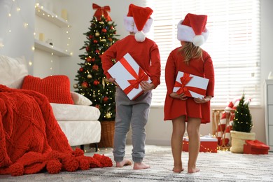 Photo of Little children in Santa hats with Christmas gifts at home, back view