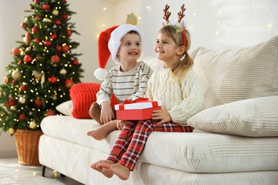 Happy children with Christmas gift on sofa at home