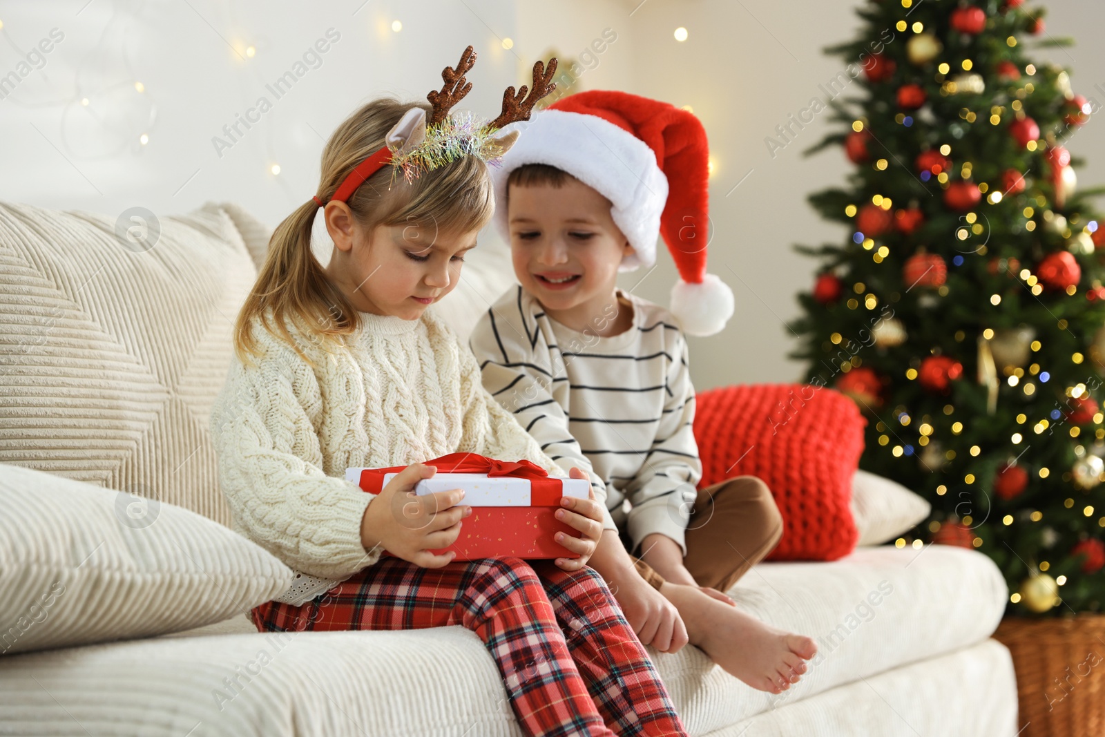 Photo of Little children with Christmas gift on sofa at home