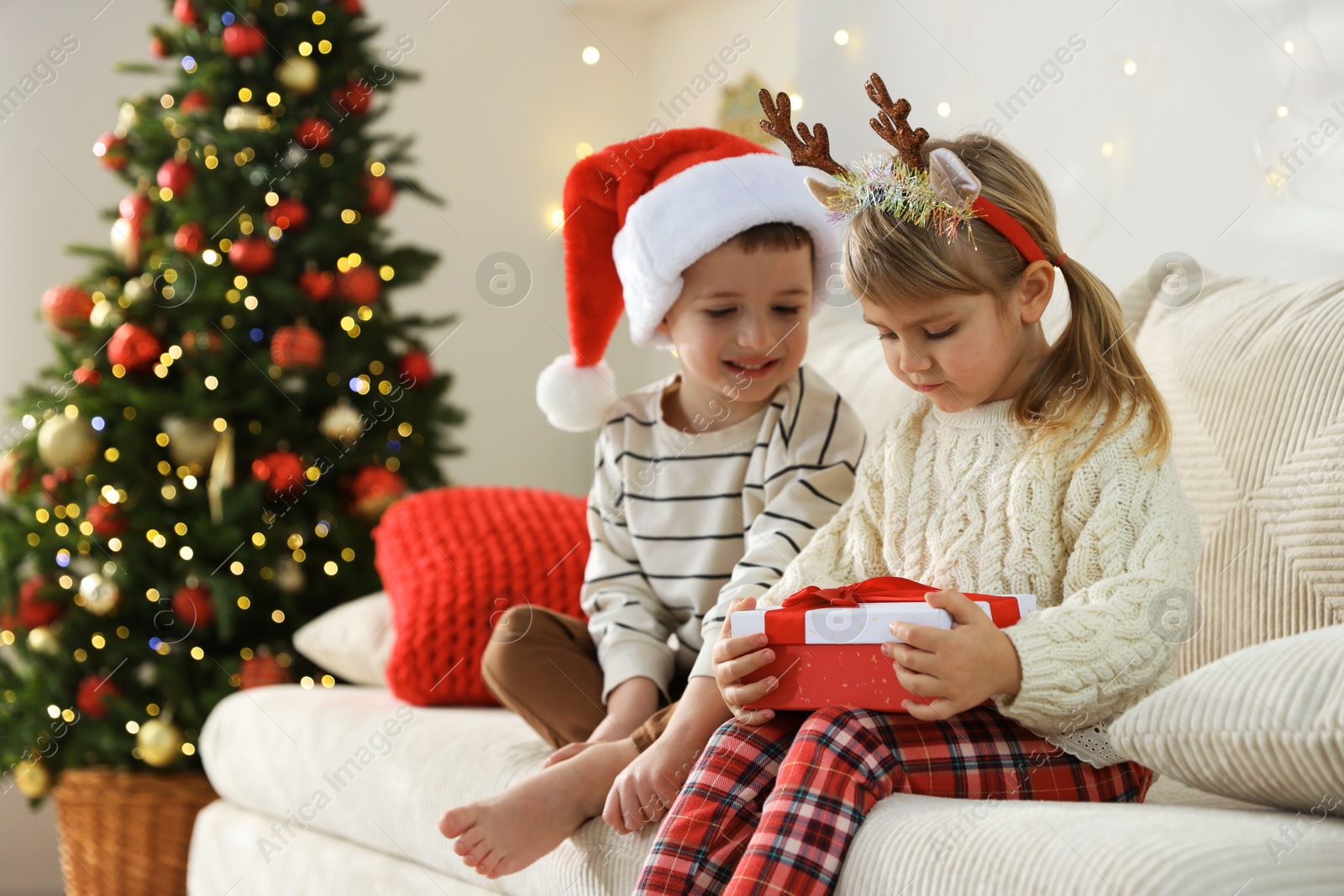 Photo of Little children with Christmas gift on sofa at home