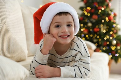 Photo of Happy little boy in Santa hat on sofa at home