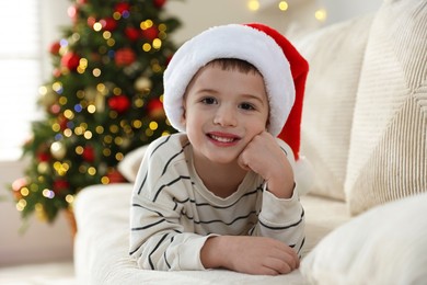 Photo of Happy little boy in Santa hat on sofa at home