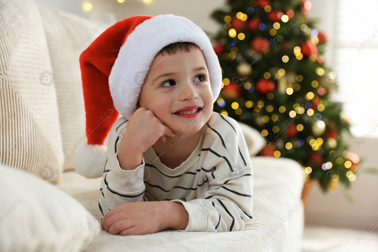 Photo of Happy little boy in Santa hat on sofa at home