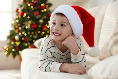 Photo of Happy little boy in Santa hat on sofa at home