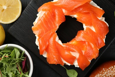 Photo of Delicious bagel with salmon and cream cheese n black table, top view