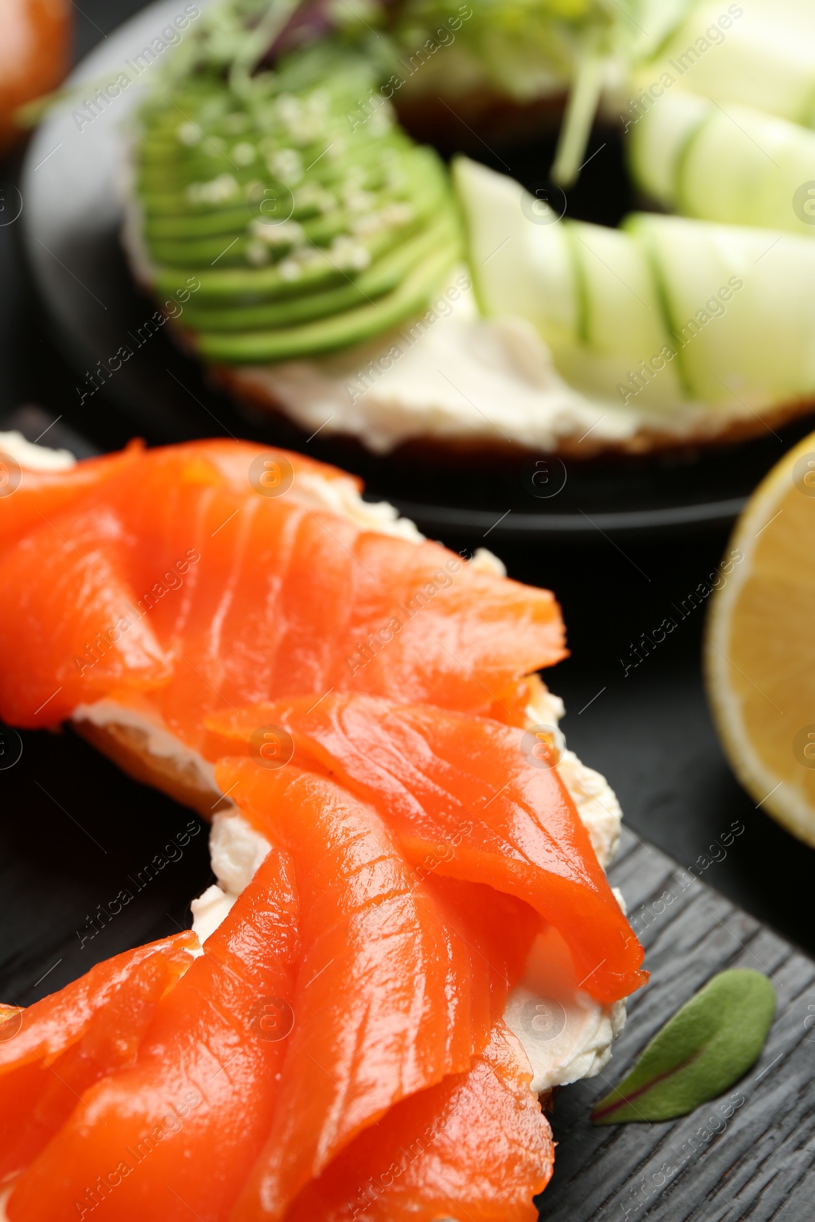 Photo of Delicious bagels with salmon and vegetables on black table, selective focus