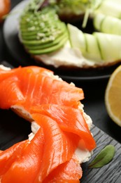 Photo of Delicious bagels with salmon and vegetables on black table, selective focus