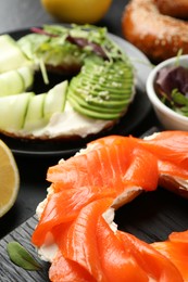 Photo of Delicious bagels with salmon and vegetables on black table, selective focus