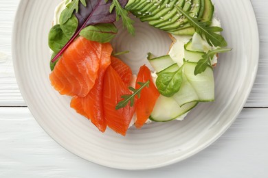 Photo of Delicious bagel with salmon, cream cheese, cucumber and avocado on white wooden table, top view