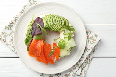 Photo of Delicious bagel with salmon, cream cheese, cucumber and avocado on white wooden table, top view