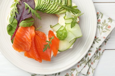 Photo of Delicious bagel with salmon, cream cheese, cucumber and avocado on white wooden table, top view