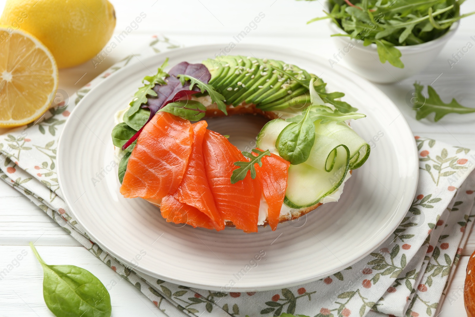 Photo of Delicious bagel with salmon, cream cheese, cucumber and avocado on white wooden table, closeup