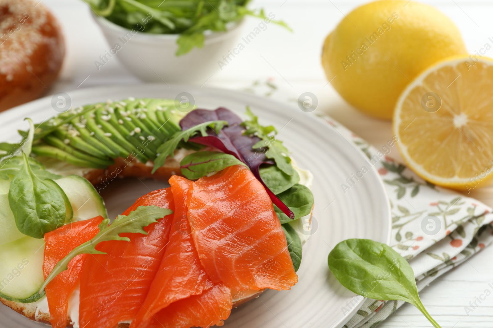 Photo of Delicious bagel with salmon, cream cheese, cucumber and avocado on white wooden table, closeup