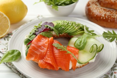 Photo of Delicious bagel with salmon, cream cheese, cucumber and avocado on white wooden table, closeup