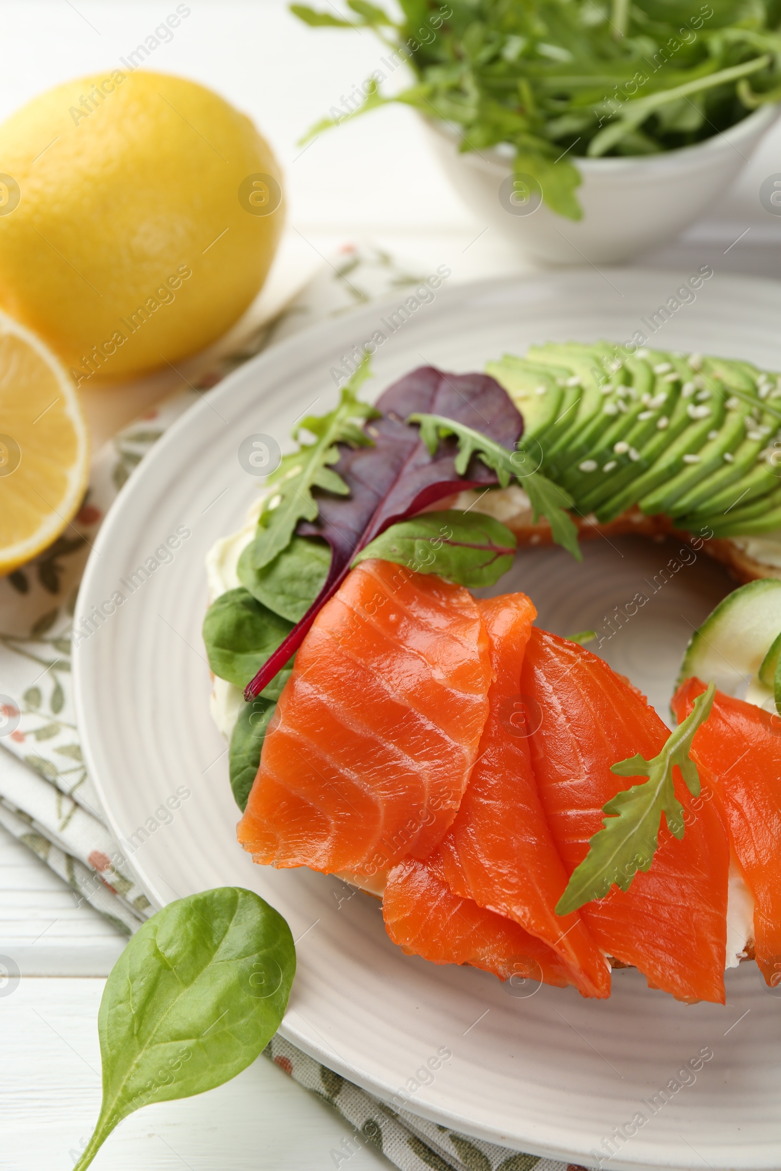 Photo of Delicious bagel with salmon, cream cheese, cucumber and avocado on white wooden table, closeup