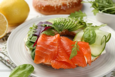 Photo of Delicious bagel with salmon, cream cheese, cucumber and avocado on white wooden table, closeup