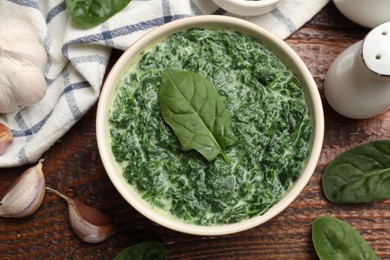 Delicious spinach sauce in bowl and spices on wooden table, flat lay