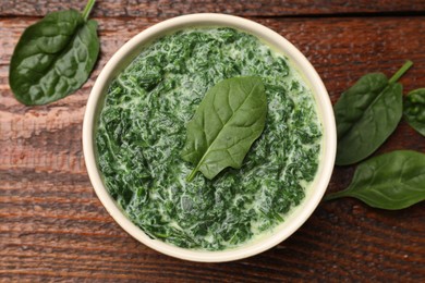 Photo of Delicious spinach sauce in bowl and leaves on wooden table, flat lay