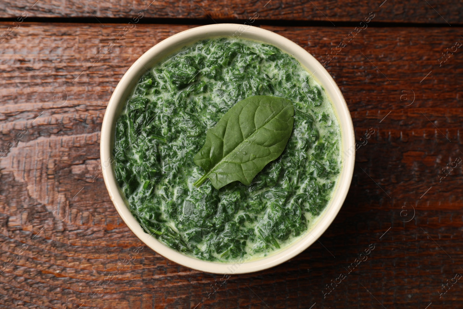 Photo of Delicious spinach sauce in bowl on wooden table, top view