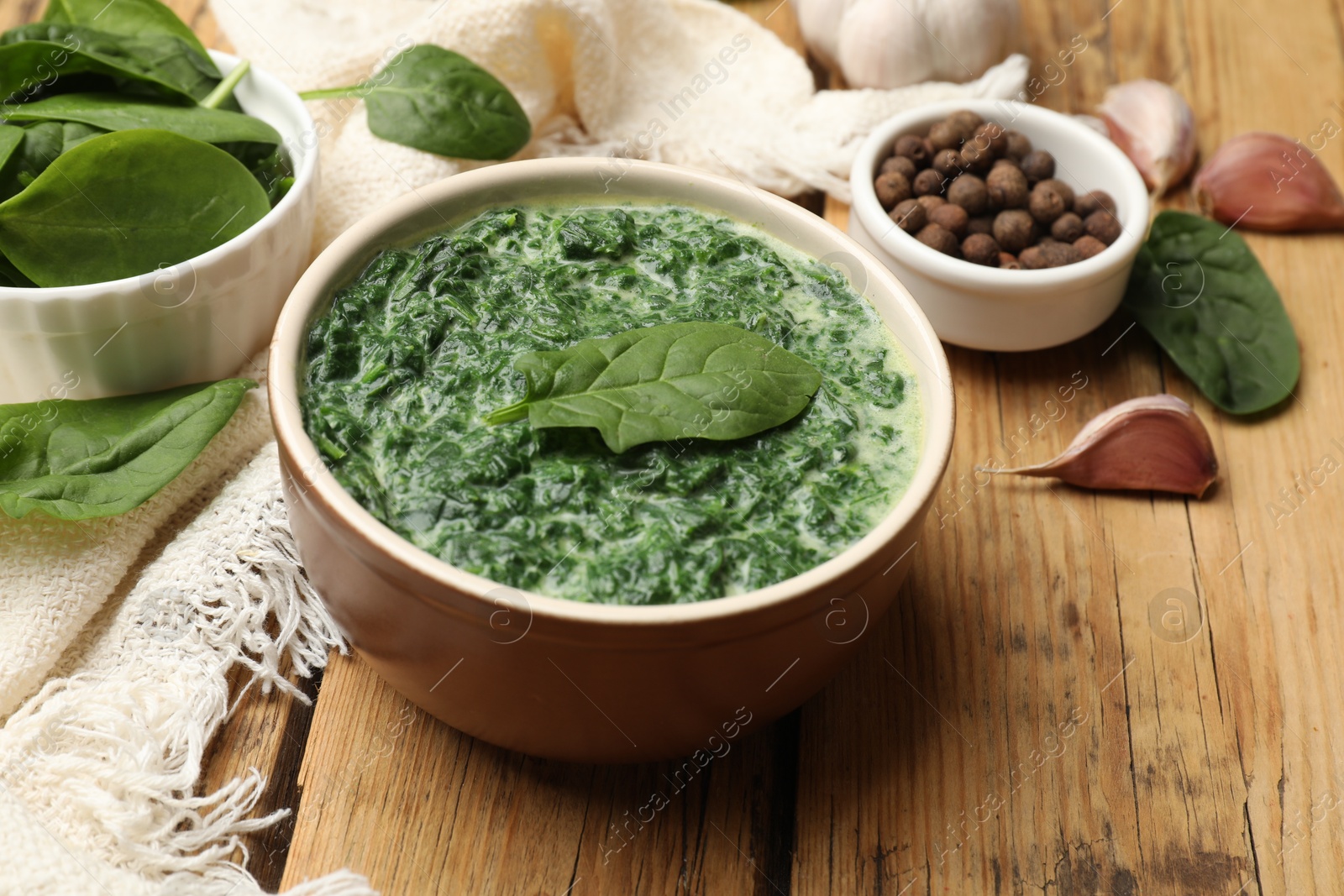 Photo of Delicious spinach sauce in bowl and spices on wooden table, closeup