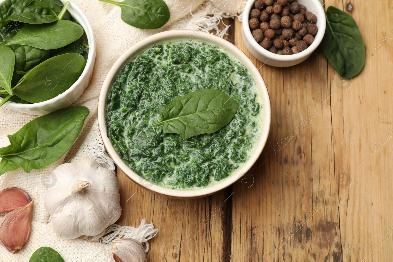 Photo of Delicious spinach sauce in bowl and spices on wooden table, flat lay. Space for text