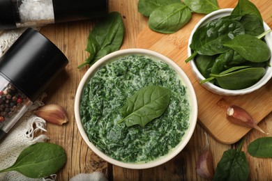 Photo of Delicious spinach sauce in bowl and spices on wooden table, flat lay