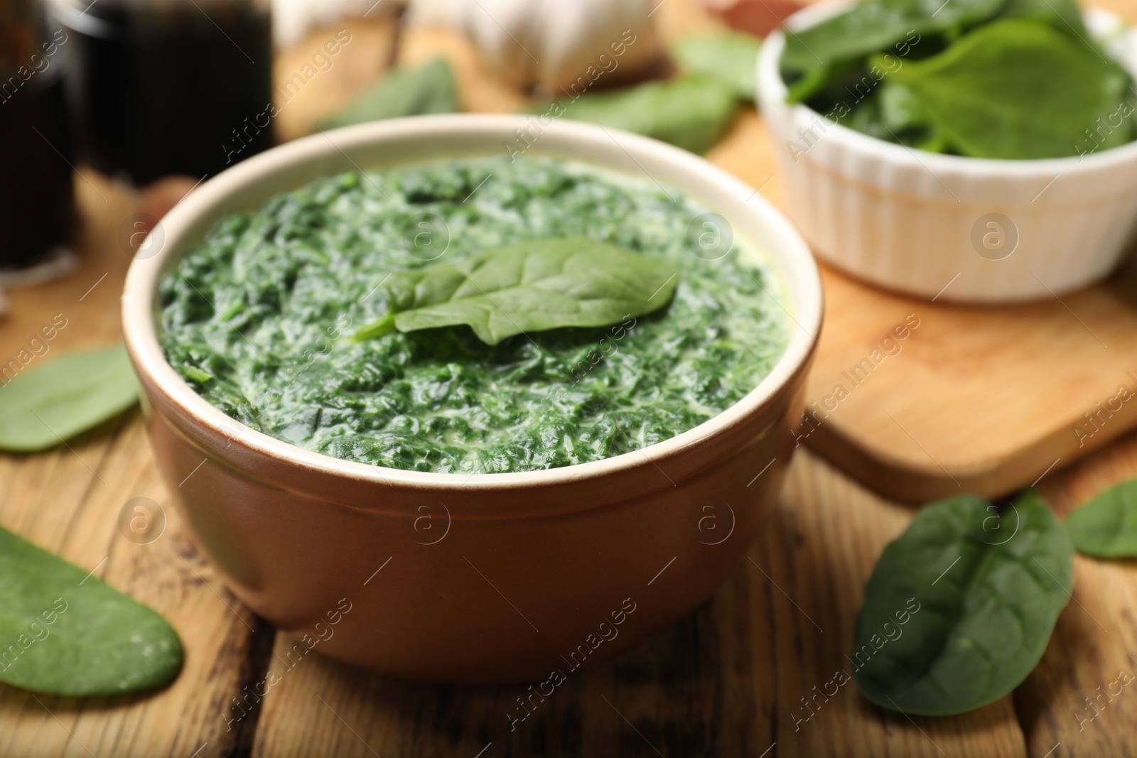 Photo of Delicious spinach sauce in bowl and leaves on wooden table, closeup