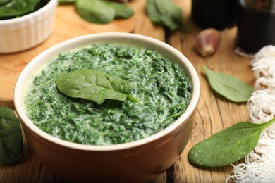 Photo of Delicious spinach sauce in bowl and leaves on wooden table, closeup