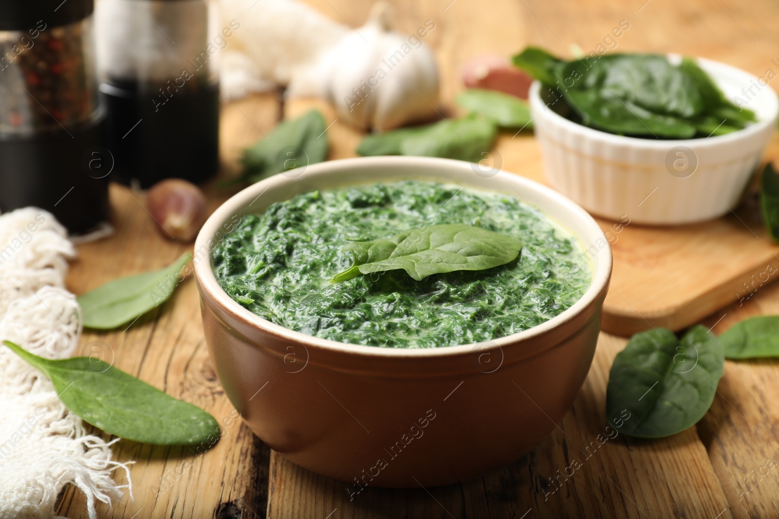 Photo of Delicious spinach sauce in bowl and leaves on wooden table, closeup