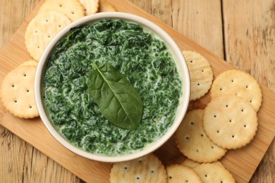 Delicious spinach sauce in bowl and crackers on wooden table, top view