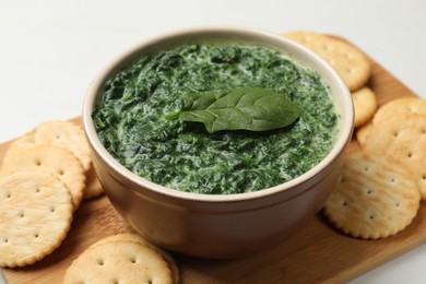 Delicious spinach sauce in bowl and crackers on table, closeup