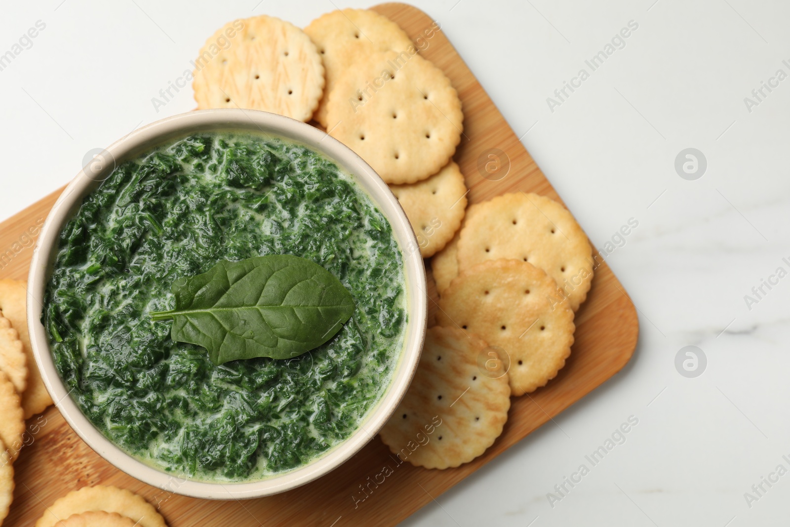 Photo of Delicious spinach sauce in bowl and crackers on white marble table, top view