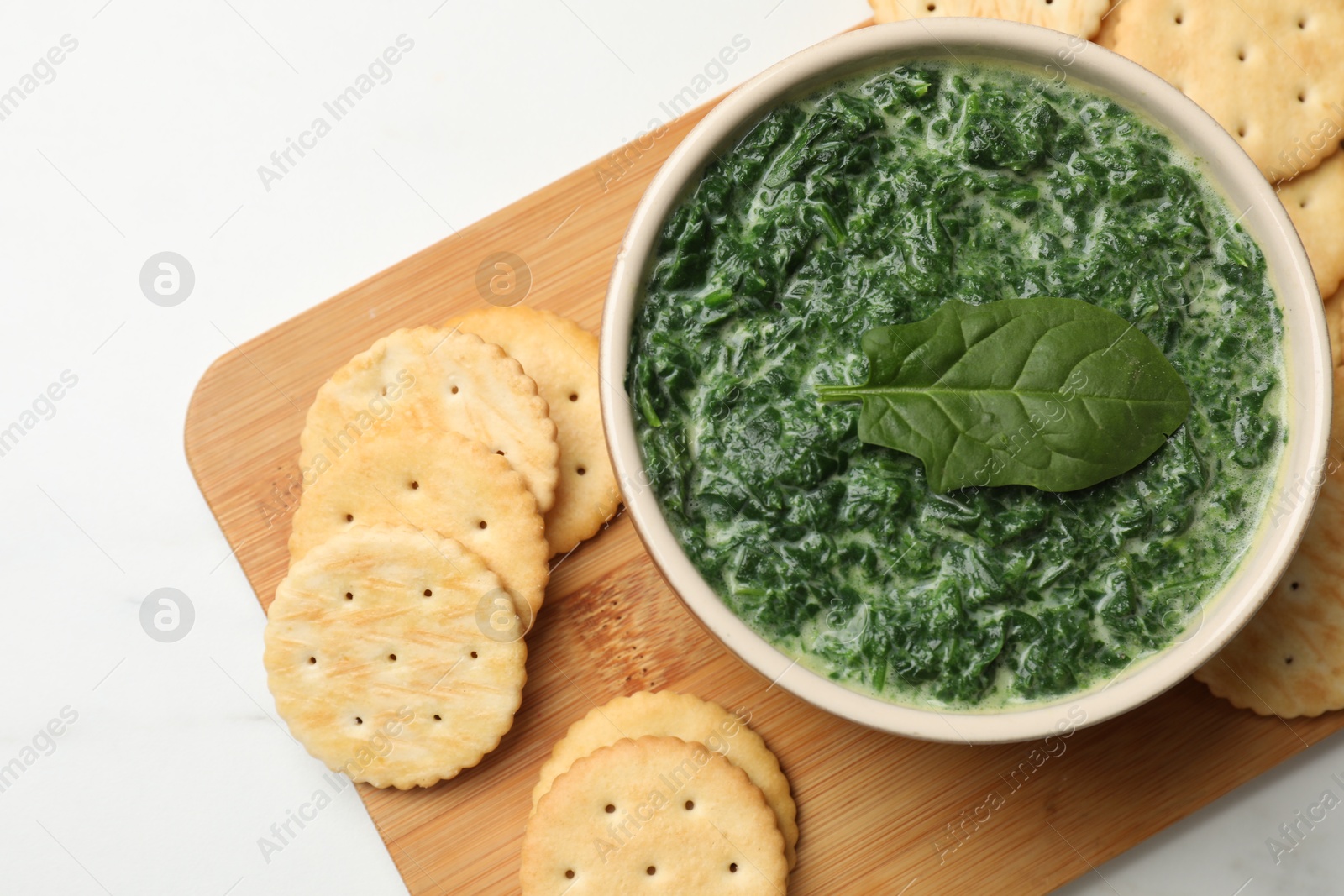 Photo of Delicious spinach sauce in bowl and crackers on white marble table, top view