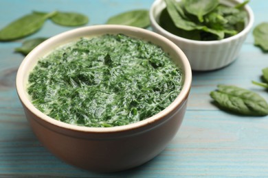 Photo of Delicious spinach sauce in bowl and leaves on light blue wooden table, closeup