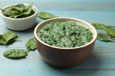 Delicious spinach sauce in bowl and leaves on light blue wooden table, closeup