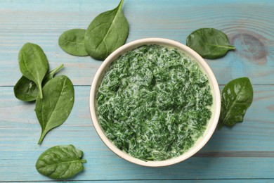 Photo of Delicious spinach sauce in bowl and leaves on light blue wooden table, flat lay