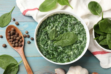 Delicious spinach sauce in bowl and spices on light blue wooden table, flat lay