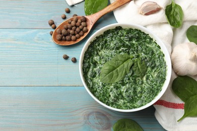 Delicious spinach sauce in bowl and spices on light blue wooden table, flat lay. Space for text