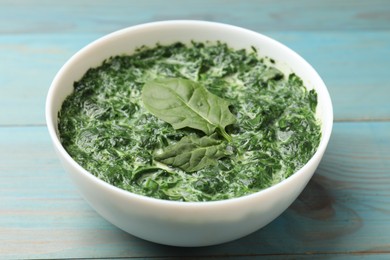 Delicious spinach sauce in bowl on light blue wooden table, closeup