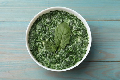 Photo of Delicious spinach sauce in bowl on light blue wooden table, top view