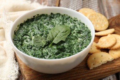 Photo of Delicious spinach sauce in bowl and crackers on table, closeup