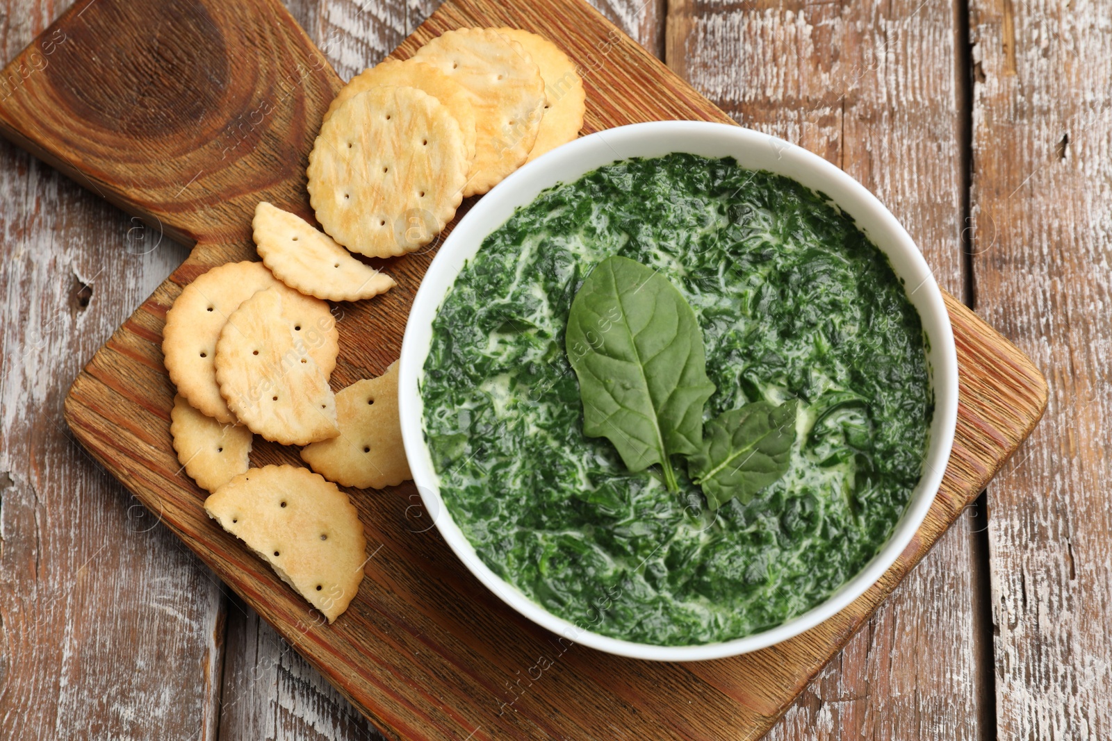 Photo of Delicious spinach sauce in bowl and crackers on wooden table, top view