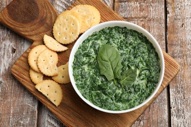 Delicious spinach sauce in bowl and crackers on wooden table, top view