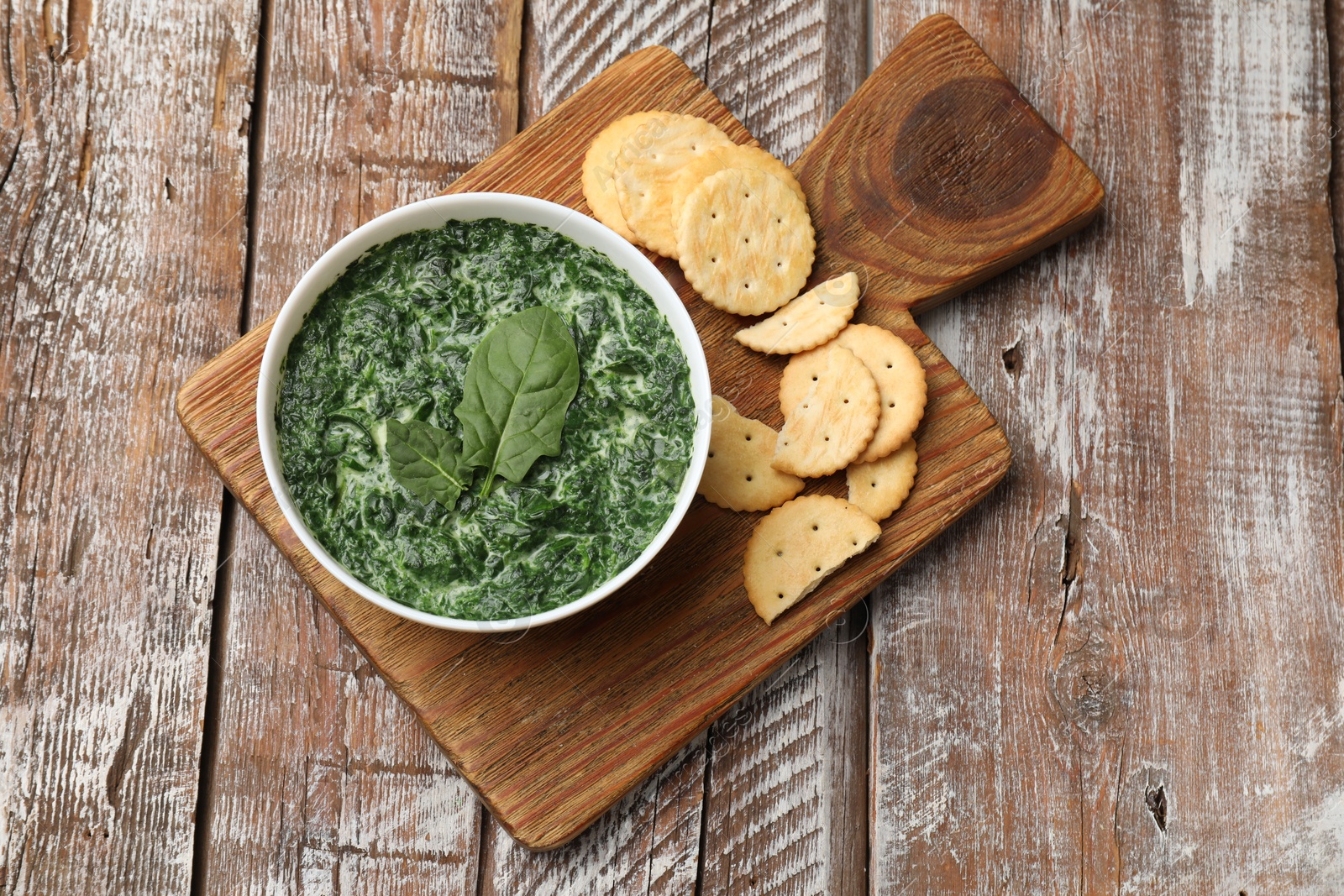 Photo of Delicious spinach sauce in bowl and crackers on wooden table, top view