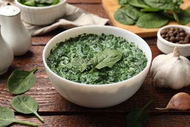 Delicious spinach sauce in bowl and spices on wooden table, closeup